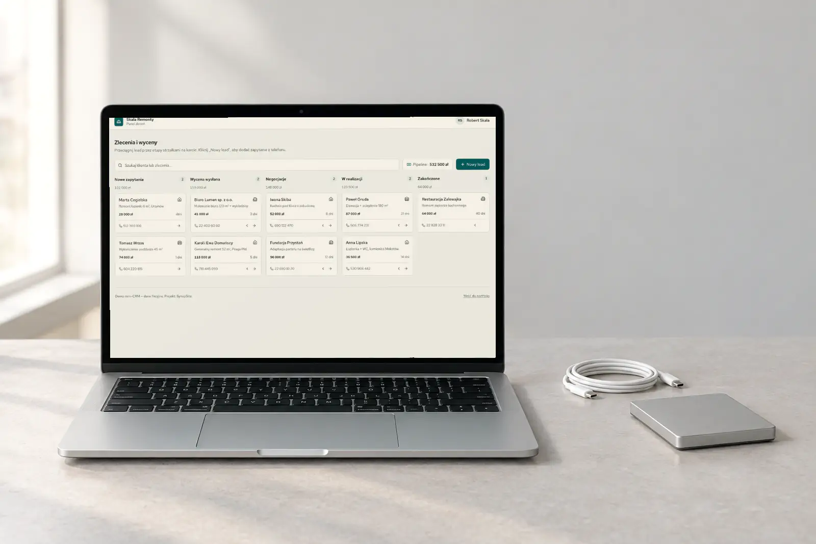 Mini-CRM Skala Remonty z lejkiem zleceń na laptopie, obok zwinięty kabel i dysk zewnętrzny.